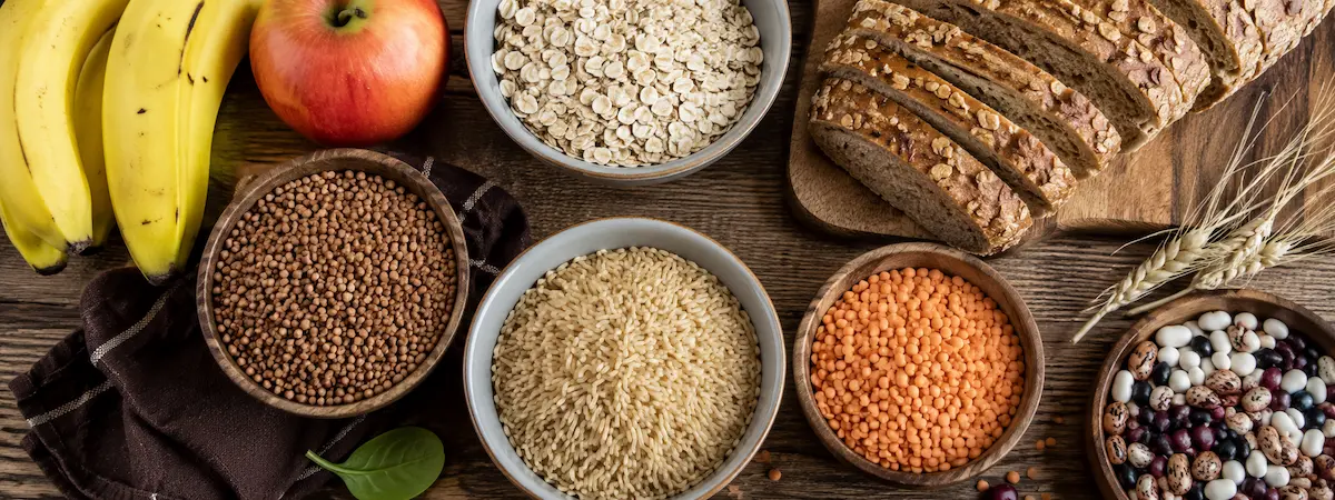 Продукты, богатые углеводами: крупы, цельнозерновой хлеб, бобовые и фрукты на столе